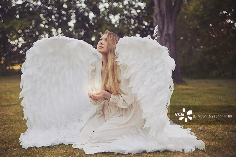 在傍晚的森林里，一位穿着天使服装的女士手持蜡烛图片素材