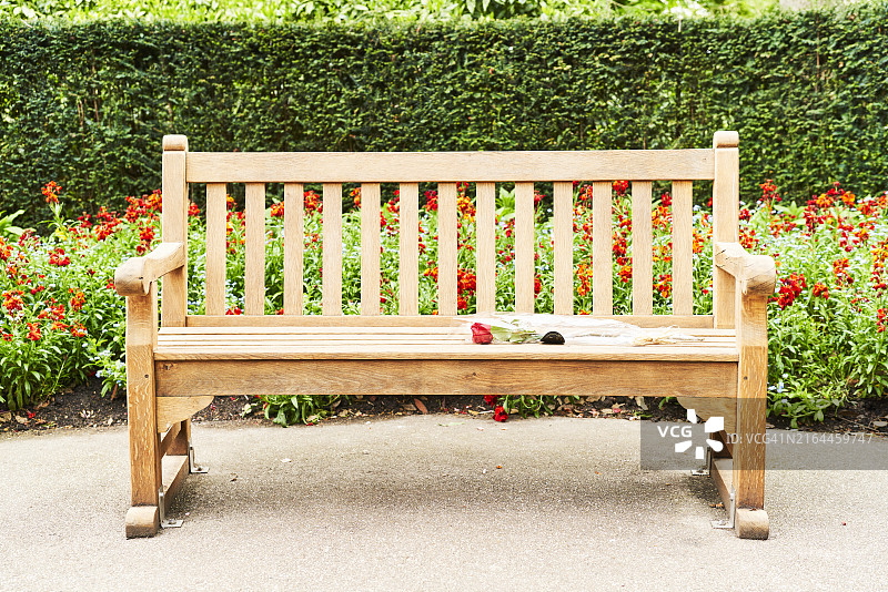 雕刻留言和红玫瑰的木制长椅，背景是红色开花植物和灌木墙图片素材