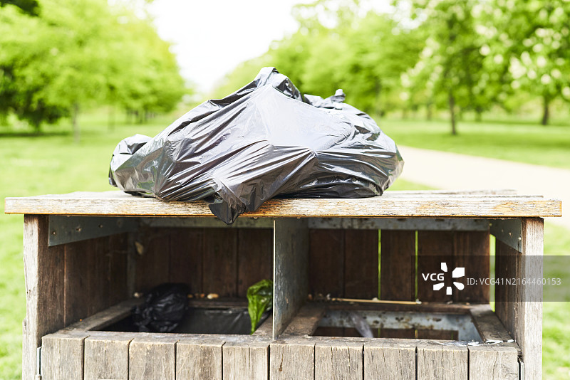 黑色塑料袋前视图：垃圾箱，背景是公园图片素材