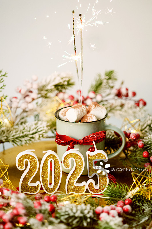 新年贺卡。2025年蜡烛、可可棉花糖杯和装饰桌上的烟花特写及留白图片素材