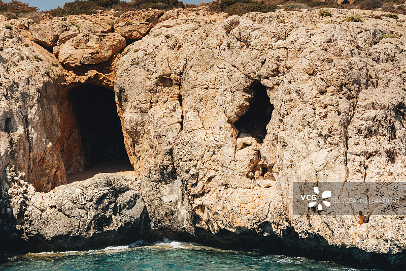 阳光明媚的清澈碧绿水域附近的岩石海岸洞穴图片素材