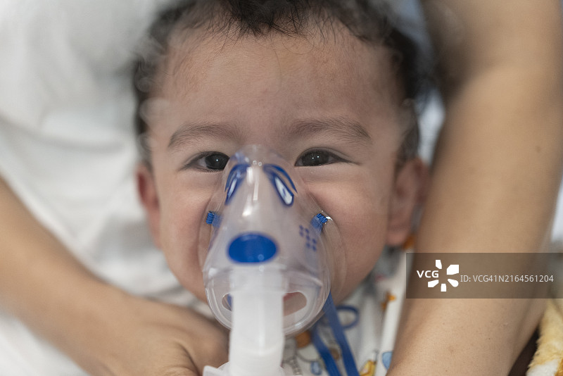 亚洲母亲手持拥抱哭泣的幼儿儿子，用雾化器面罩进行吸入药物治疗图片素材