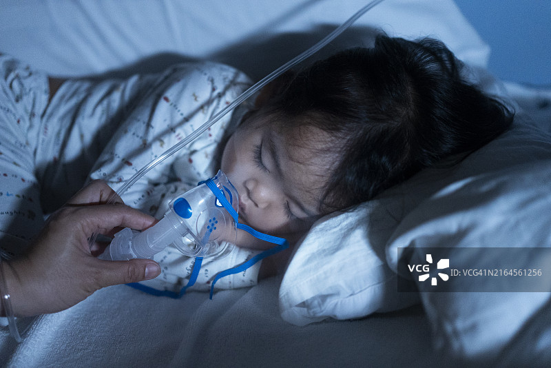 亚洲母亲手持拥抱哭泣的幼儿儿子，用雾化器面罩进行吸入药物治疗图片素材