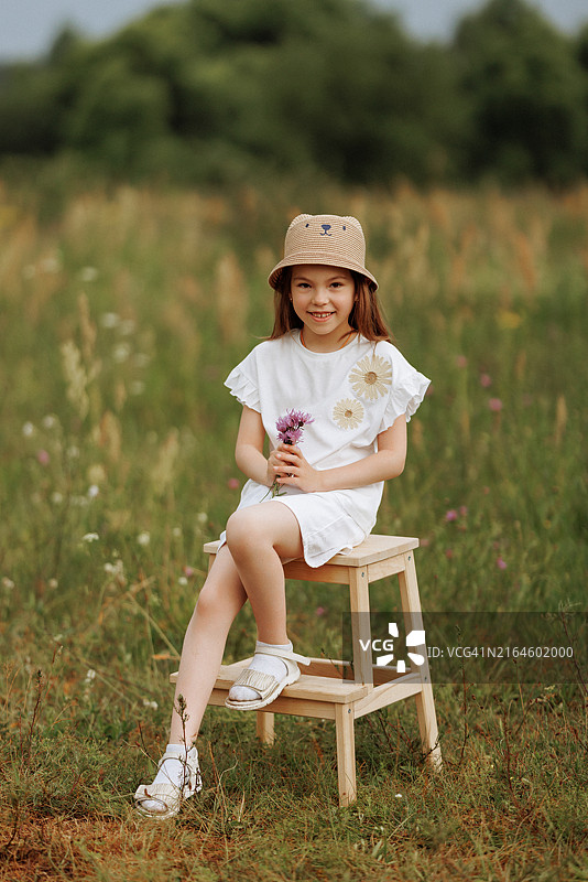 坐在田野里的木凳上，手持鲜花的年轻女孩图片素材