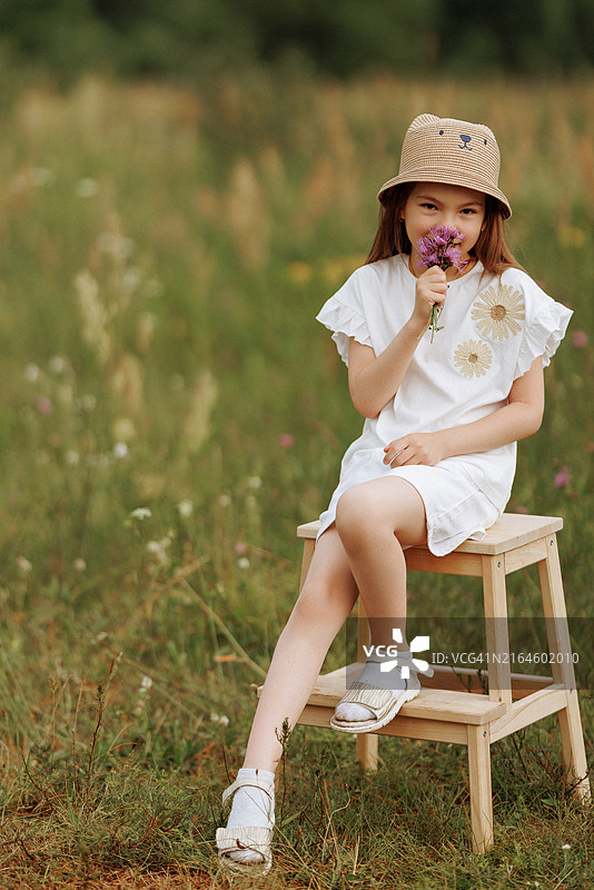 坐在田野里的木凳上，手持鲜花的年轻女孩图片素材