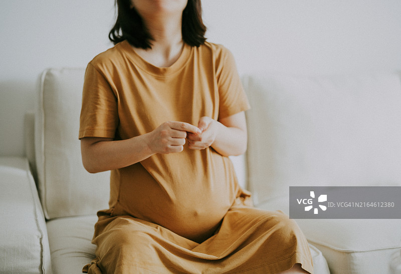 年轻的亚洲孕妇坐在沙发上吃坚果图片素材