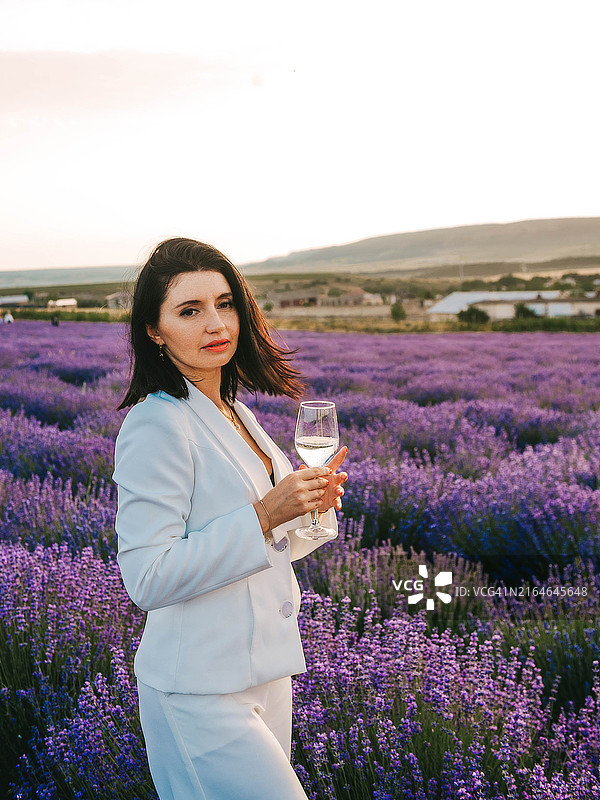在薰衣草田野餐，女性端着装有葡萄酒或水的玻璃杯图片素材