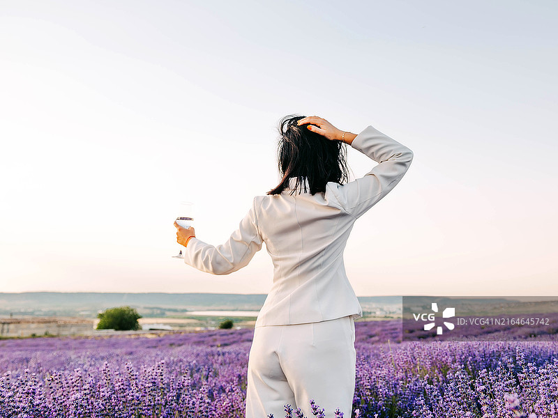 在薰衣草田野餐，女性端着装有葡萄酒或水的玻璃杯图片素材