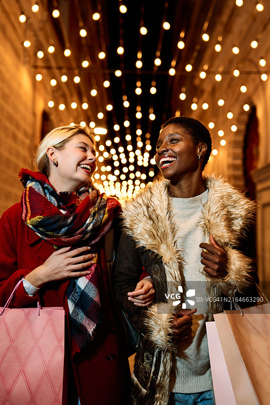 两位年轻女人在夜晚节日彩灯下欢笑购物图片素材