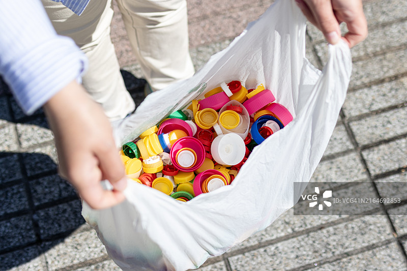 女人手拿着用塑料瓶盖装满的塑料袋准备回收图片素材