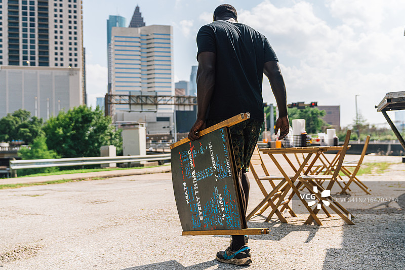 在德克萨斯州休斯顿，拍摄一位食品车老板搬运并设置一个A字框架菜单板，为烟熏烧烤食品车做准备图片素材