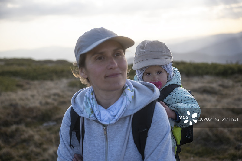 日落时分，妈妈和孩子在背包里徒步旅行的写真图片素材