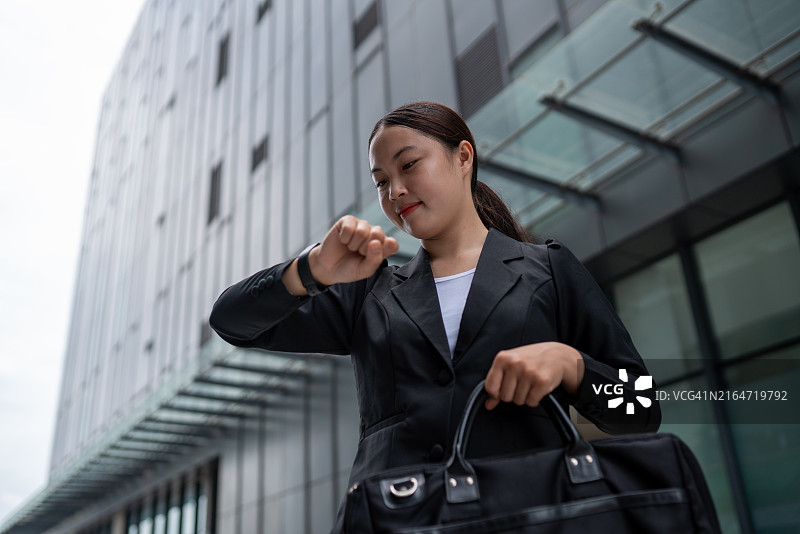 身穿黑色西装、携带黑色钱包的女商人正在看她的手表图片素材