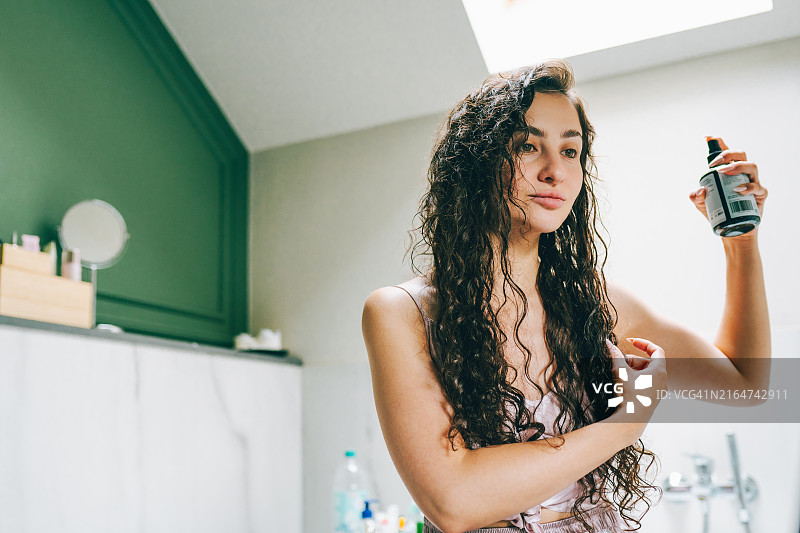 卷发护理：女人用精油在家打理头发图片素材