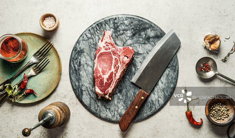 大理石砧板上带厨房刀、香草和香料的生猪排图片素材