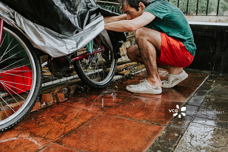 男人匆忙跑出家门，迅速遮盖自行车以防雨淋，他没解开鞋带就匆忙穿上鞋子图片素材