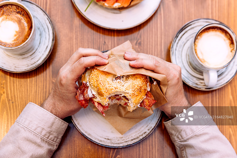 男人吃培根奶油奶酪煎蛋面包圈，个人视角图片素材