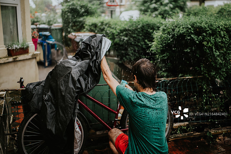 男子在暴雨中用防雨罩锁好停在潮湿前院的自行车图片素材