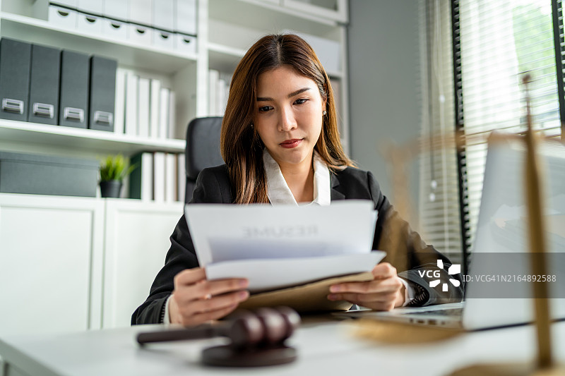 亚洲女律师在法庭上使用锤子和天平。有魅力的法官在办公室的桌子上查看文件图片素材