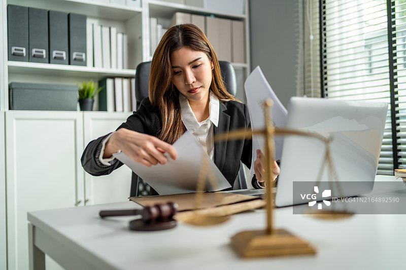 亚洲女律师在法庭上使用锤子和天平。有魅力的法官在办公室的桌子上查看文件图片素材