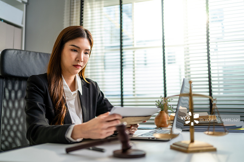 亚洲女律师在法庭上使用锤子和天平。有魅力的法官在办公室的桌子上查看文件图片素材