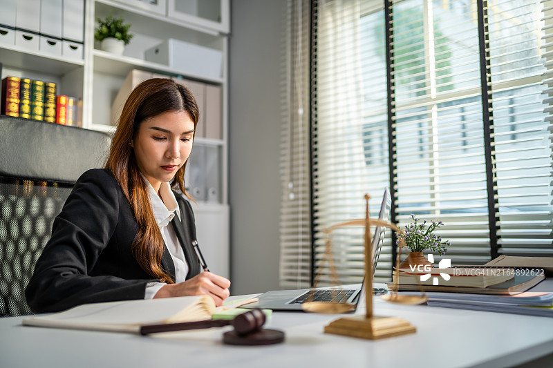 亚洲女律师在法庭上使用锤子和天平。有魅力的法官在办公室的桌子上查看文件图片素材