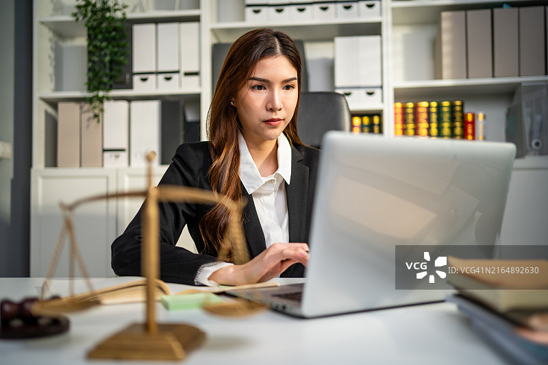 亚洲女律师在法庭上使用锤子和天平。有魅力的法官在办公室的桌子上查看文件图片素材