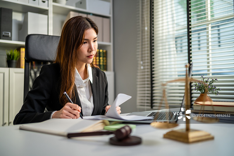 亚洲女律师在法庭上使用锤子和天平。有魅力的法官在办公室的桌子上查看文件图片素材