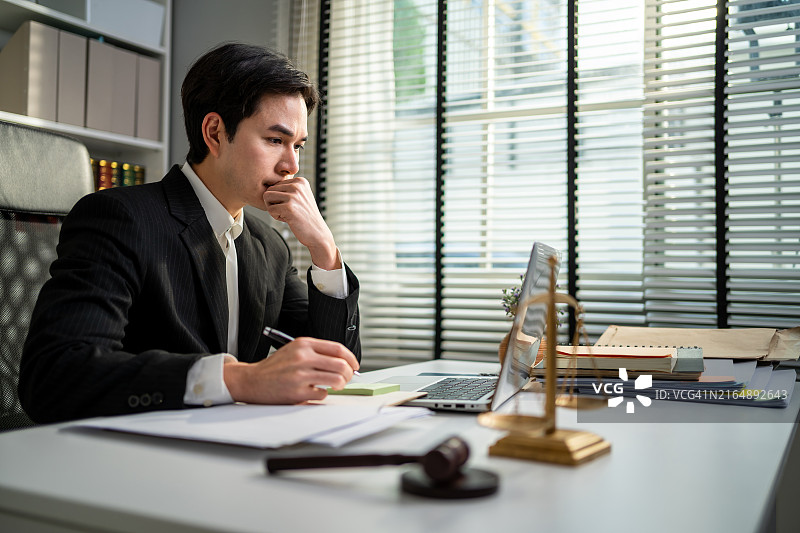 亚洲男律师在法庭上使用锤子和正义天平工作，有魅力的法官律师坐在桌旁，看着办公室里的纸质文件，法律和法律商业服务概念图片素材