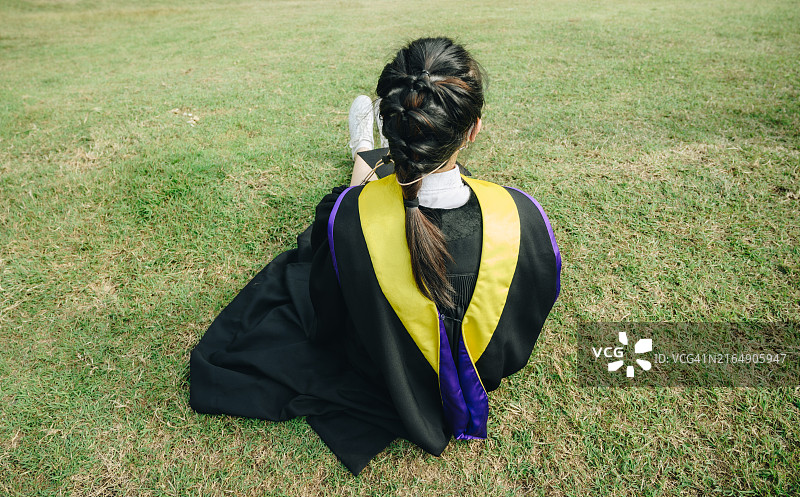 坐在绿地上身穿毕业礼服的亚洲女学生背影图片素材