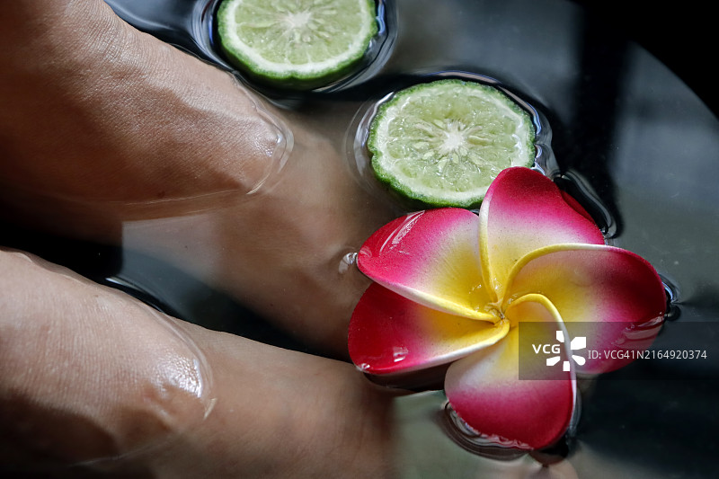 女子在水疗中心将双脚浸泡在漂浮着鸡蛋花的水中。女性在健康中心接受修脚护理的特写镜头。图片素材