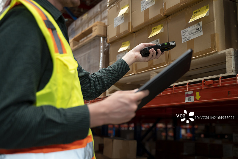 年轻的仓库工人用便携式扫描仪扫描货架上的产品包装盒图片素材