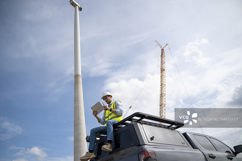 佩戴安全带的智能工程师在风车工厂、风力涡轮机农场现场工作图片素材