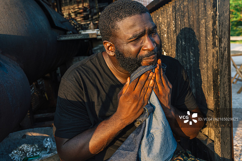 坚韧的餐车老板擦拭着脸上的汗水，坐在烧烤拖车后图片素材
