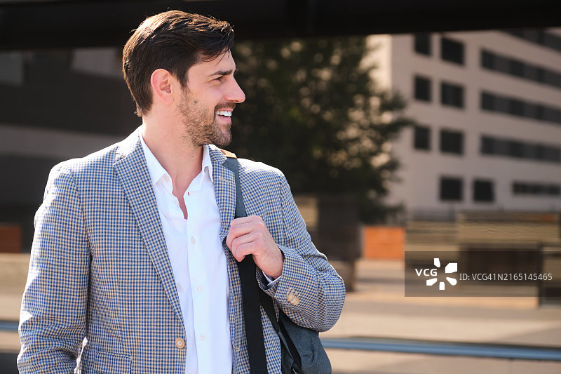 在办公楼外手持背包微笑行走的商人图片素材