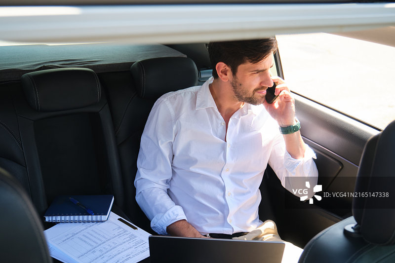 在车里打电话和使用笔记本电脑的商人图片素材
