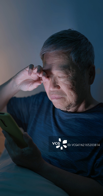 老人滚动智能手机暗色背景图片素材