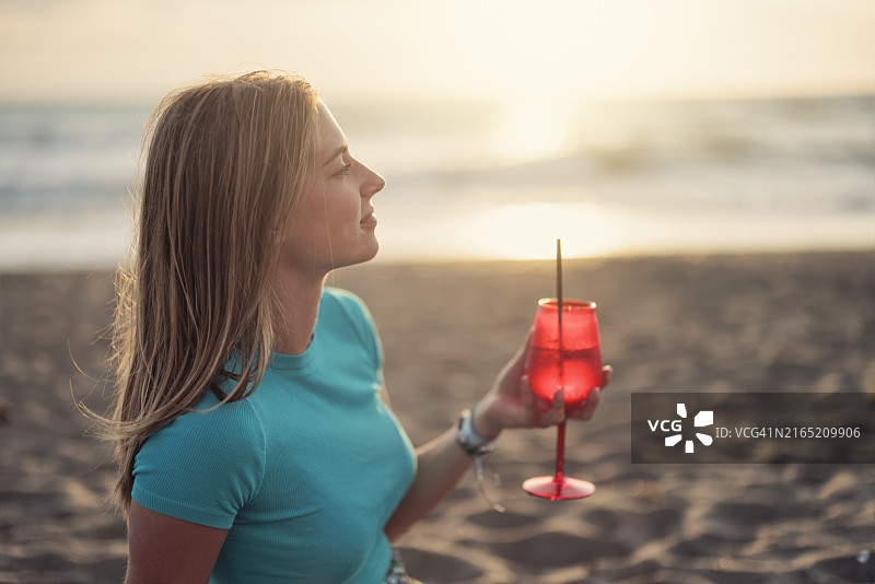 年轻女人在托斯卡纳海滩日落时畅饮图片素材