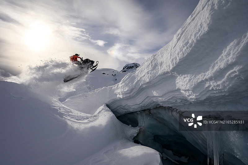 野外雪地摩托车手在冰洞前跳跃图片素材