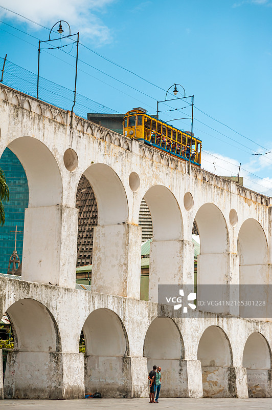 两名男子在拉帕高架渠前交谈，有轨电车从上方驶过图片素材
