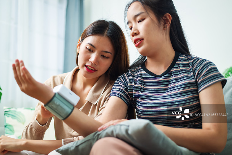 两名亚洲妇女在家中客厅互相测量血压图片素材