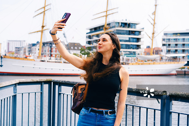 在德国不莱梅哈芬享受阳光，使用智能手机的快乐年轻女子图片素材