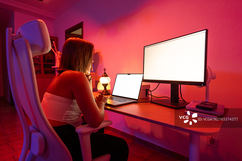 年轻女人晚上在智能彩色灯光下在家用笔记本电脑工作图片素材