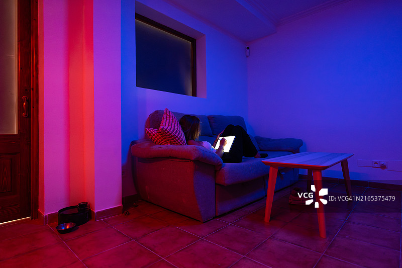 在家中使用平板电脑，在智能彩色灯光下放松的年轻女人图片素材
