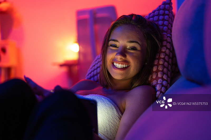 年轻女人在智能彩色灯光下沙发上使用平板放松图片素材