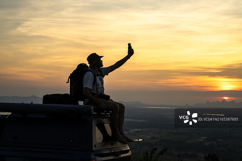 坐在车顶上用手机愉快拍照的男人图片素材