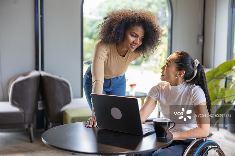 坐在轮椅上的亚洲残疾女性与非洲女性在联合办公区进行商务洽谈图片素材