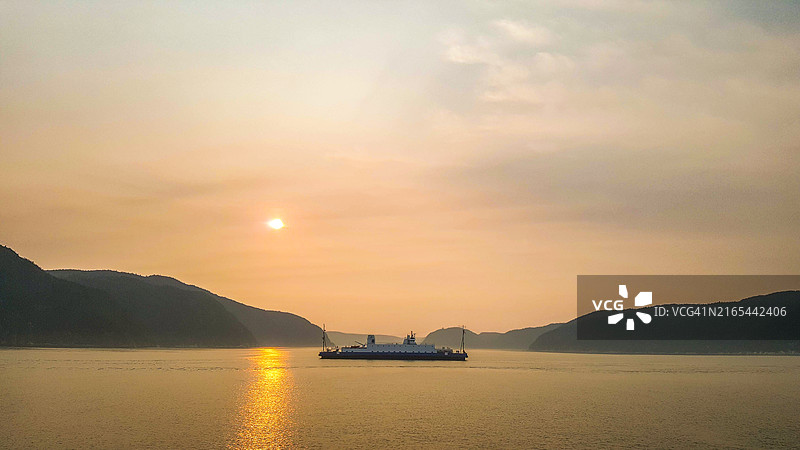 日落时分，渡轮横渡圣劳伦斯河，背景是萨格奈峡湾，加拿大魁北克图片素材