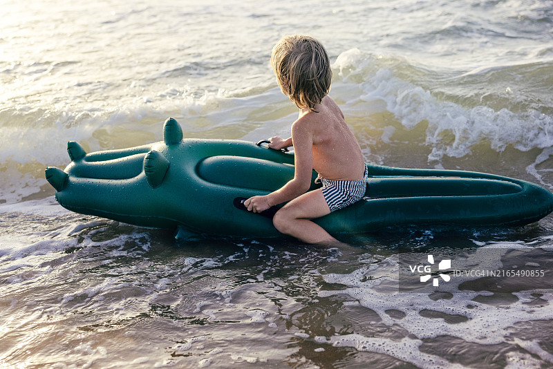 在海边拿着充气鳄鱼的小男孩图片素材