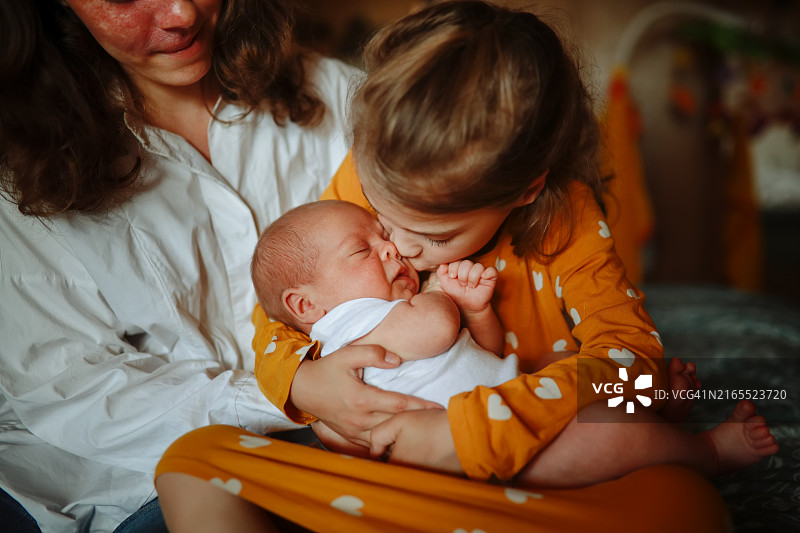舒适的家中，妈妈抱着新生婴儿和女儿的温馨时刻图片素材